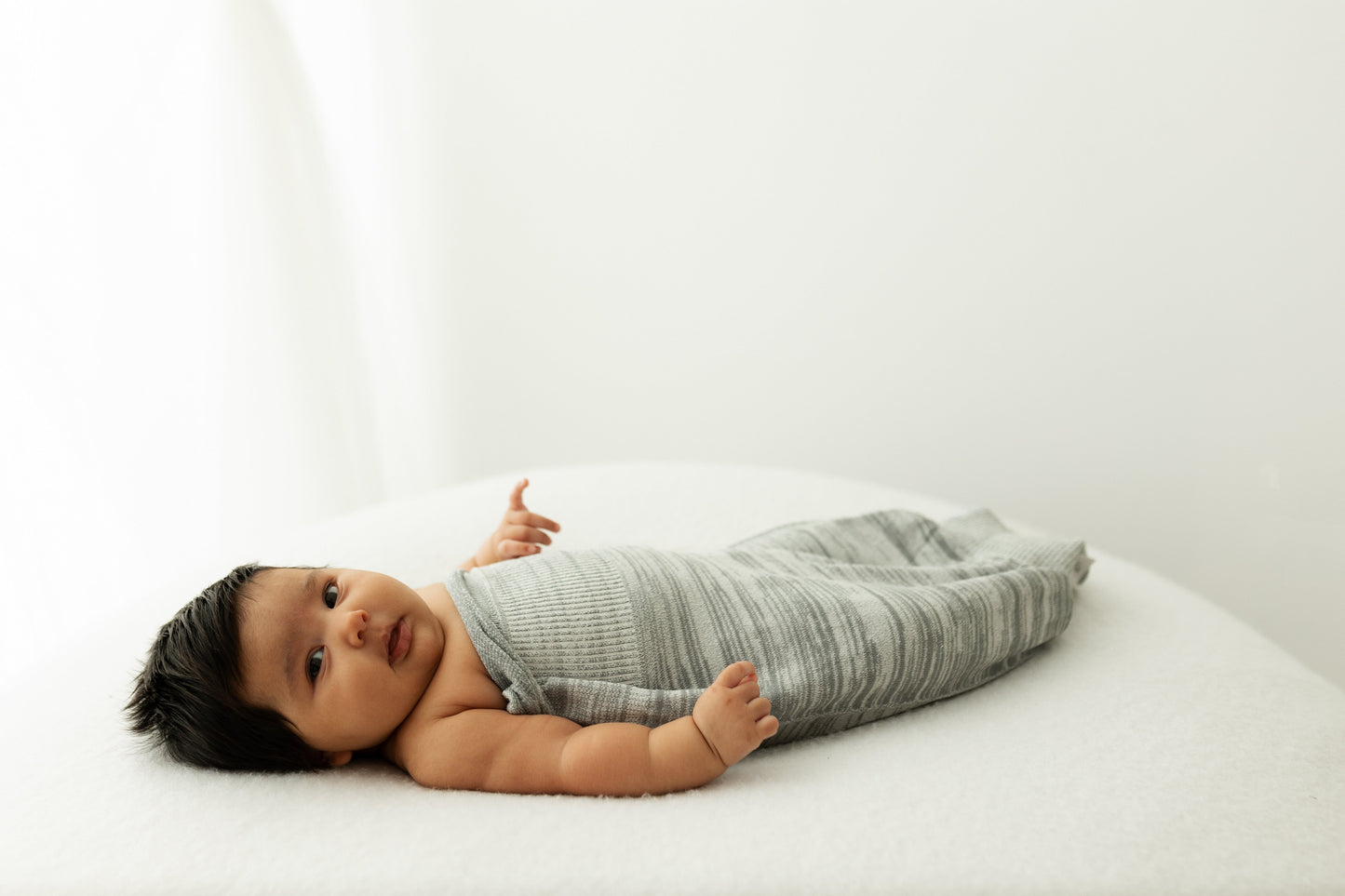 A baby resting with its arms out of its swaddle.