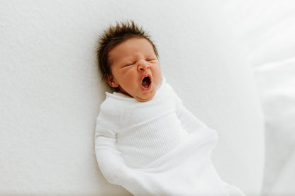 A tired baby in a white sleep sack.