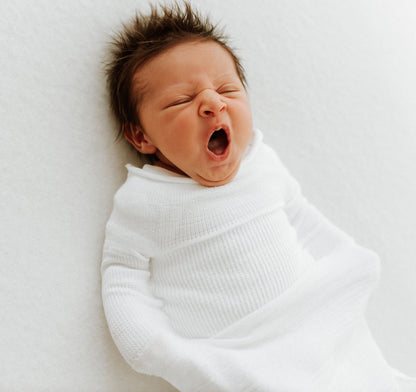 A yawning baby in a Swaddelini.