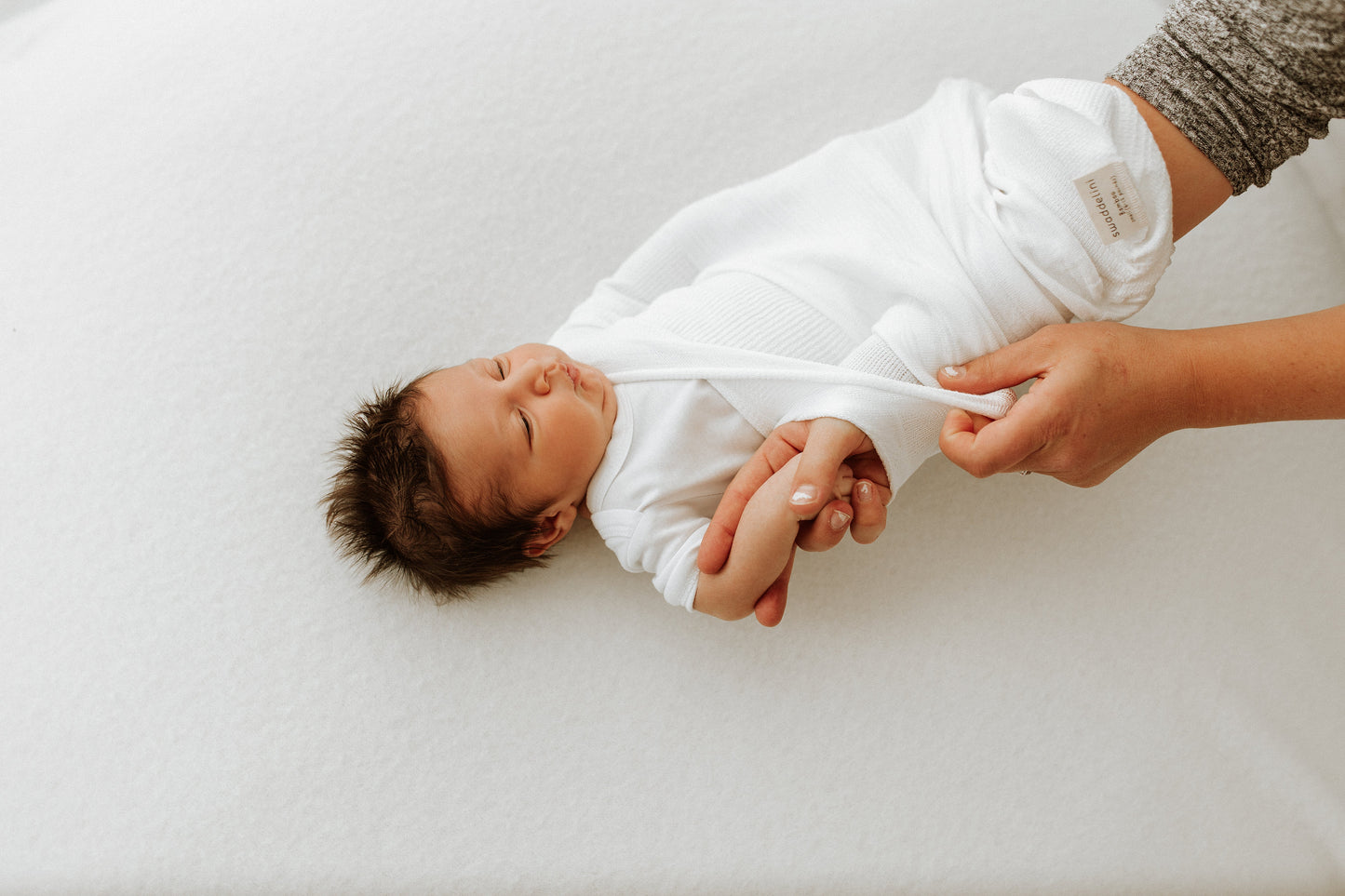 A mother putting her baby in a knit swaddle.