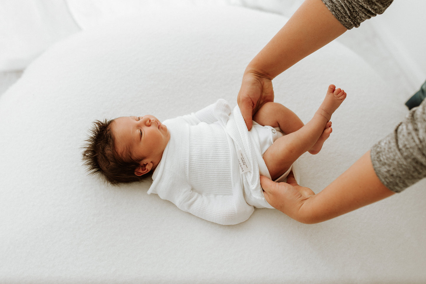 A mother accessing her baby's diaper while in a swaddle.