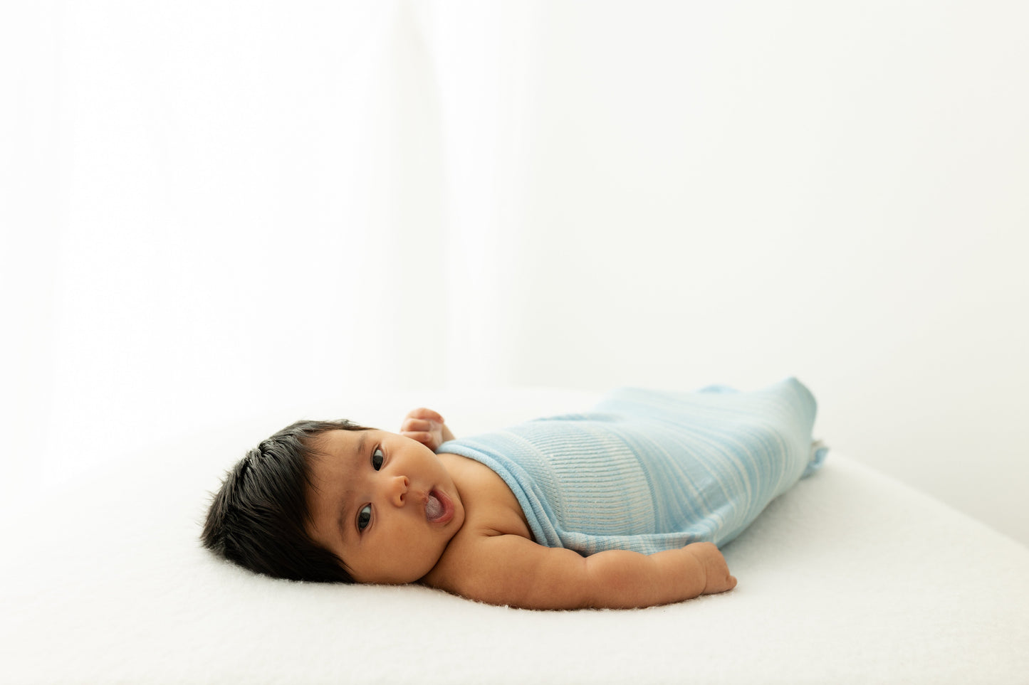 A baby lying in its sleep sack with its arms out.