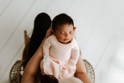 A mother holding her baby in a pink sleep sack.