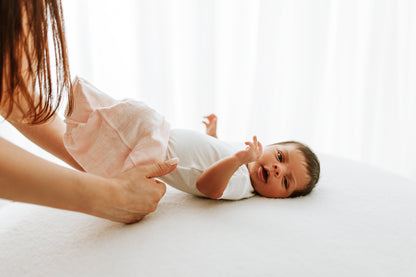 A mother putting her baby into a pink sleep sack.
